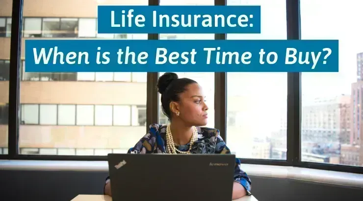 Woman in dress sitting down behind computer looking out window thinks about when the best time to buy life insurance is.